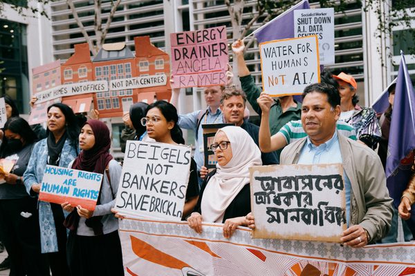 Protesters holding signs reading "Beigels Not Bankers Save Brick Lane", "Water for Humans Not AI", and "Housing Rights Are Human Rights".
