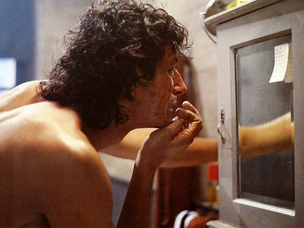 Close-up of a person with curly hair leaning against a window while smoking.