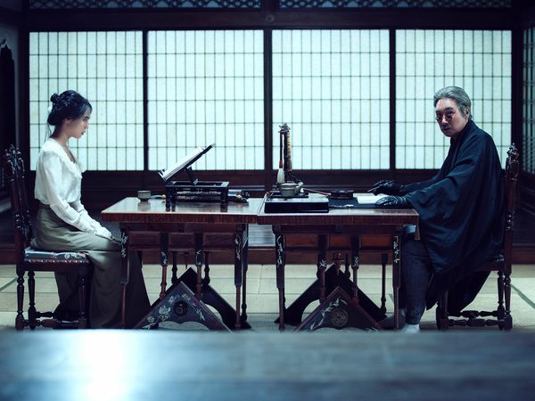 Two people, a man and a woman, sitting at a traditional Japanese desk in a room with paper screens and wooden furnishings.